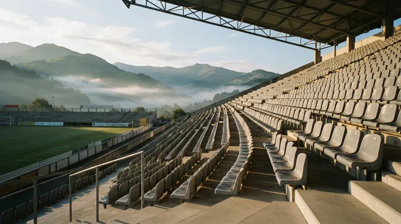 Ein leeres Stadion im Morgenlicht mit Blick auf die Sitzreihen, im Hintergrund Hügel und aufsteigender Nebel.