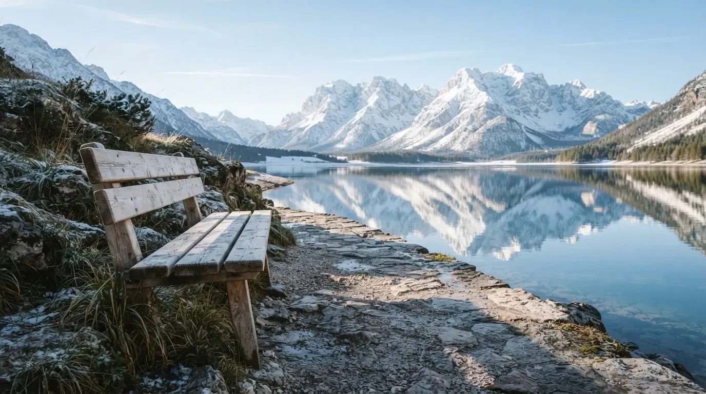 Eine Bank an einem Bergsee, dahinter schneebedeckte Gipfel im klaren Licht eines Wintermorgens.