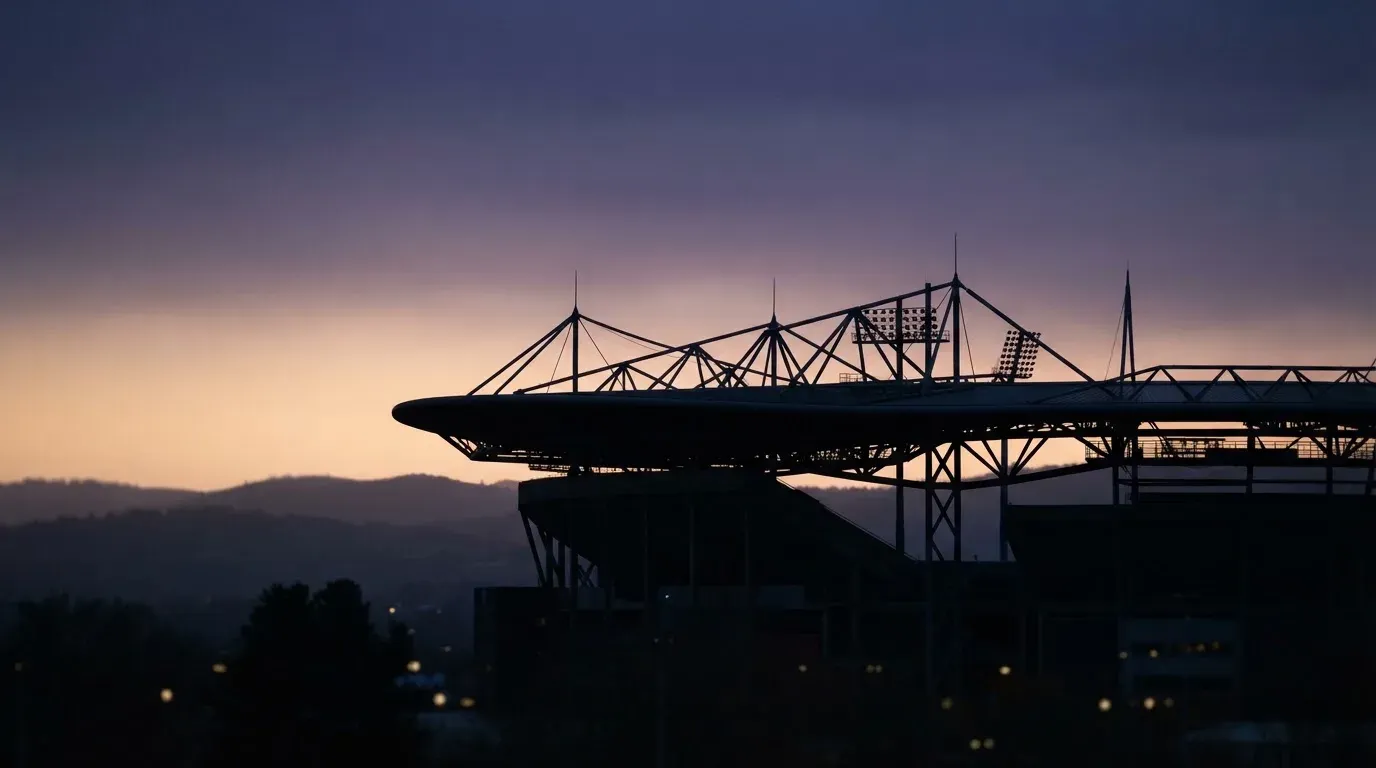Die Silhouette eines Stadiondachs vor dem violetten Abendhimmel, dahinter eine Hügelkette.