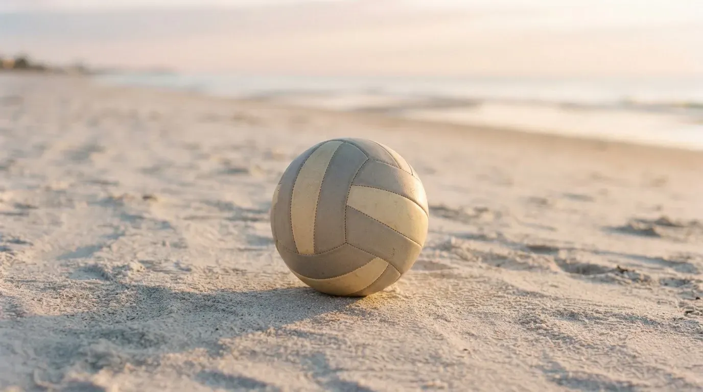 Ein Volleyball liegt auf feinem Sand an einem leeren Strand bei Sonnenaufgang.