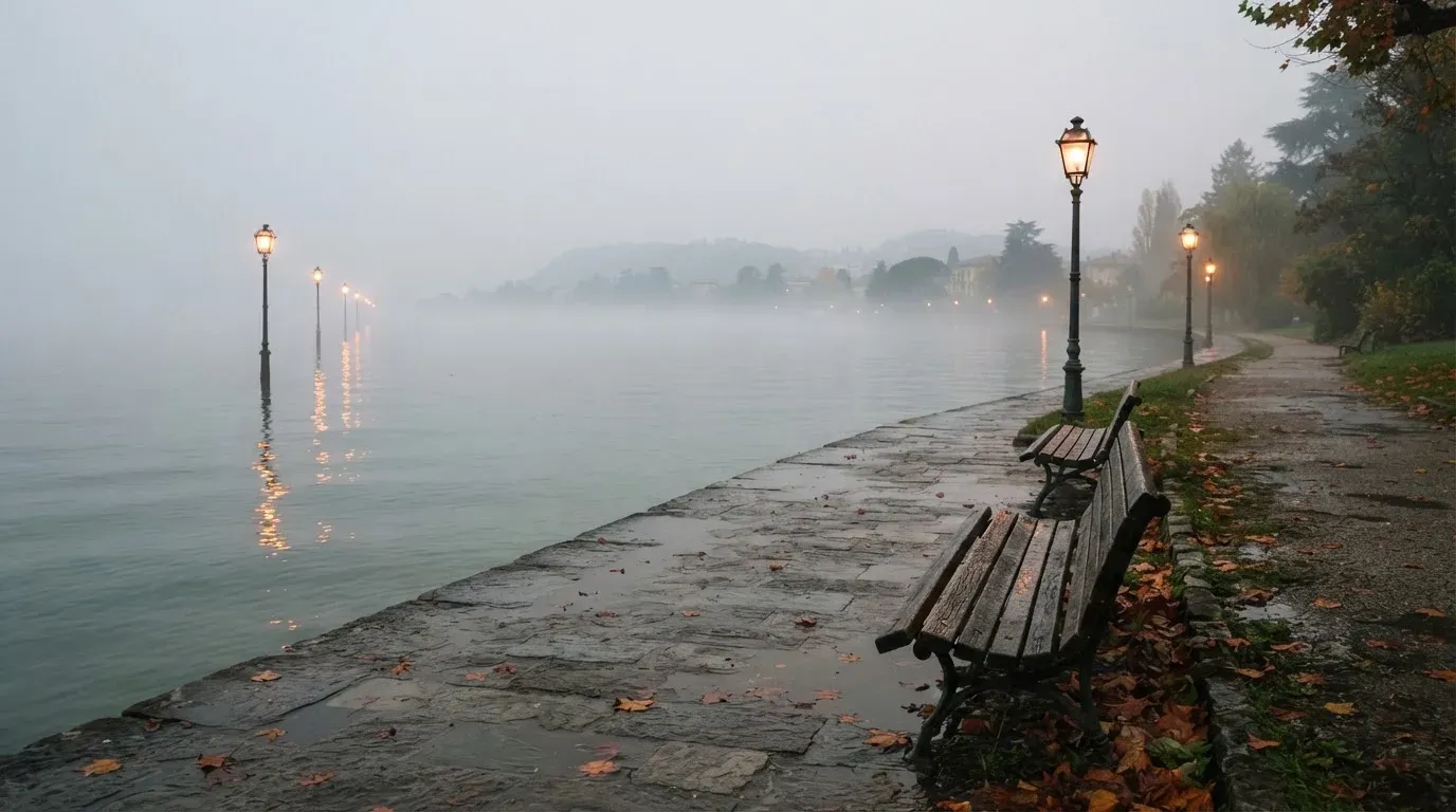 Eine Seepromenade mit leeren Bänken an einem nebligen Morgen, im Wasser spiegeln sich die Lichter der Uferlaternen.