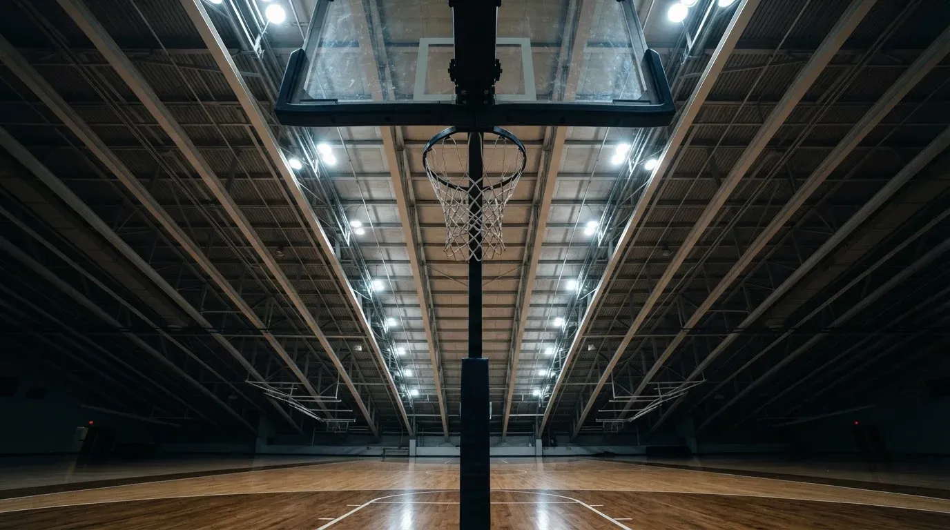 Ein Basketballkorb von unten gesehen, darüber eine Hallendecke mit Scheinwerfern und Stahlträgern.