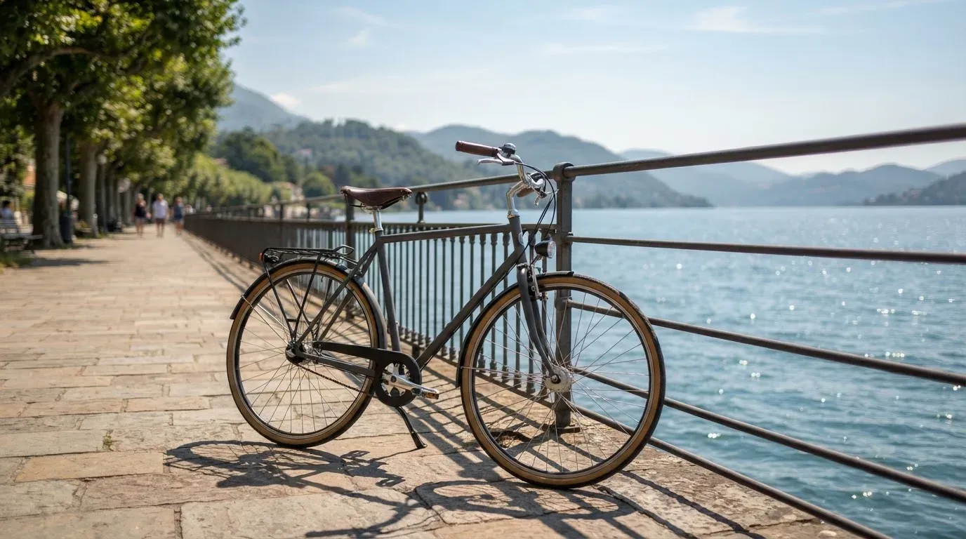 Ein Fahrrad lehnt an einem Geländer einer Uferpromenade an einem See im Sonnenlicht.
