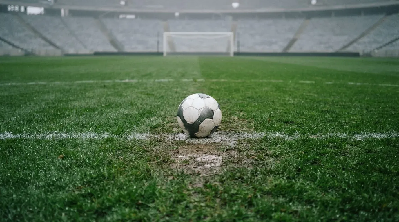 Ein einzelner Fussball liegt auf dem Elfmeterpunkt eines leeren Strafraums, der Rasen glänzt nass.