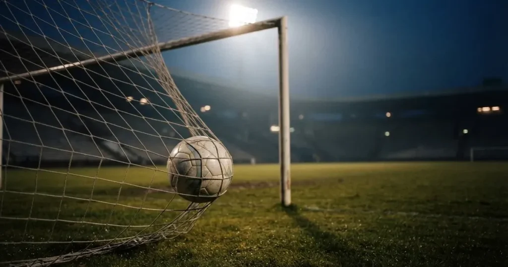 Ein Fussball liegt im Netz eines Tores, Flutlicht und kalte Abendluft liegen über dem leeren Platz