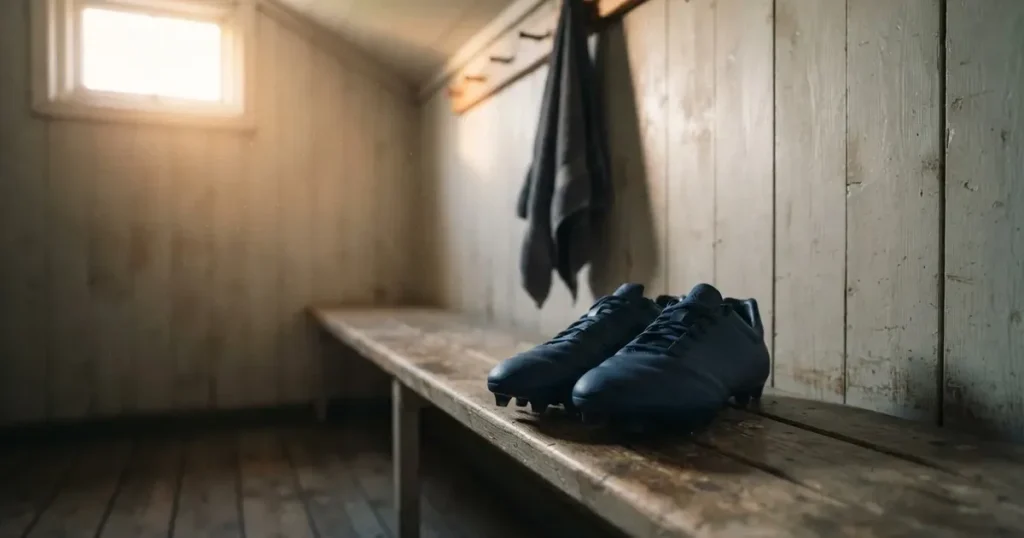Zwei Fussballschuhe stehen nebeneinander auf einer Holzbank in einer leeren Umkleidekabine.