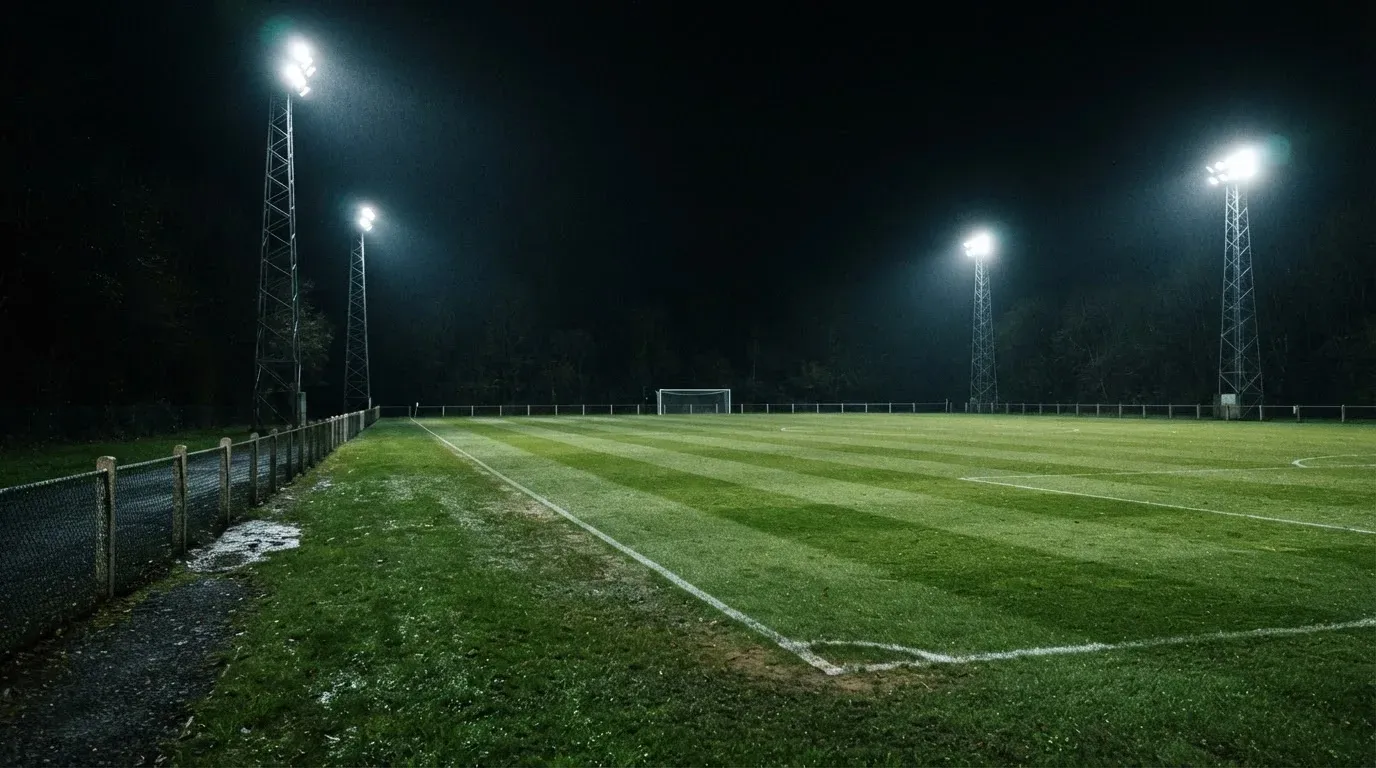 Hohe Flutlichtmasten ragen nachts über einen leeren Trainingsplatz, der Rasen glänzt im weissen Licht.
