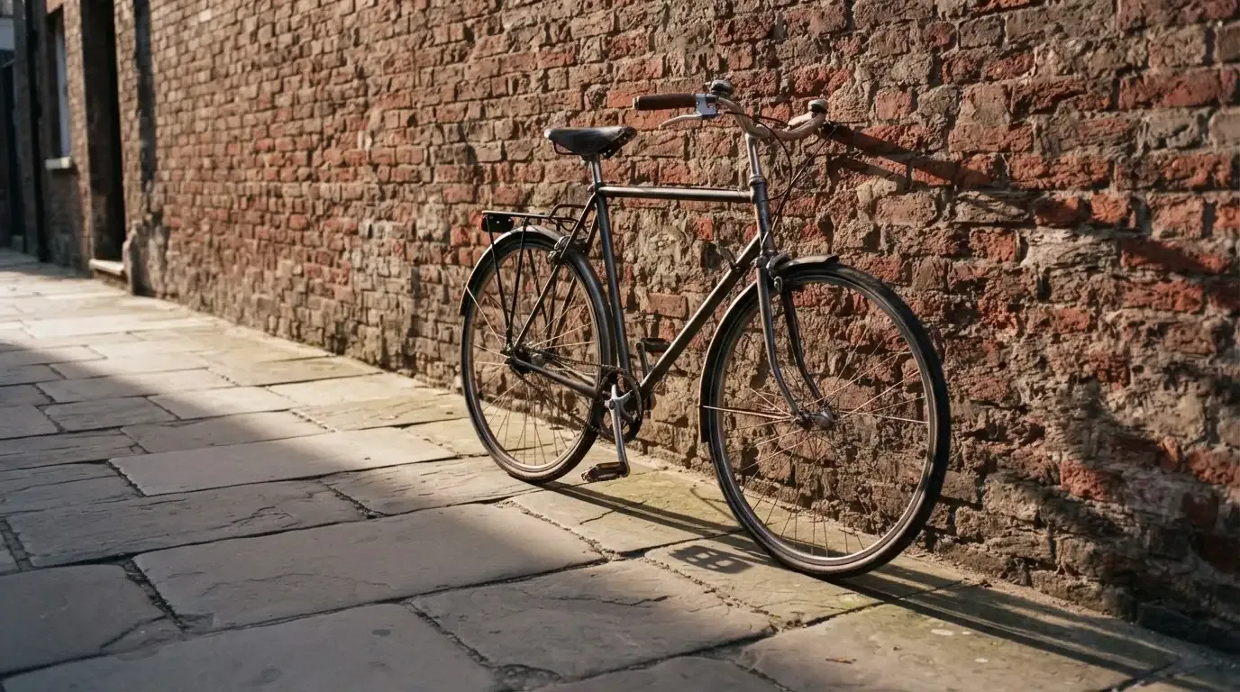 Ein Fahrrad lehnt an einer Backsteinmauer, auf dem Gehweg davor fallen lange Schatten.