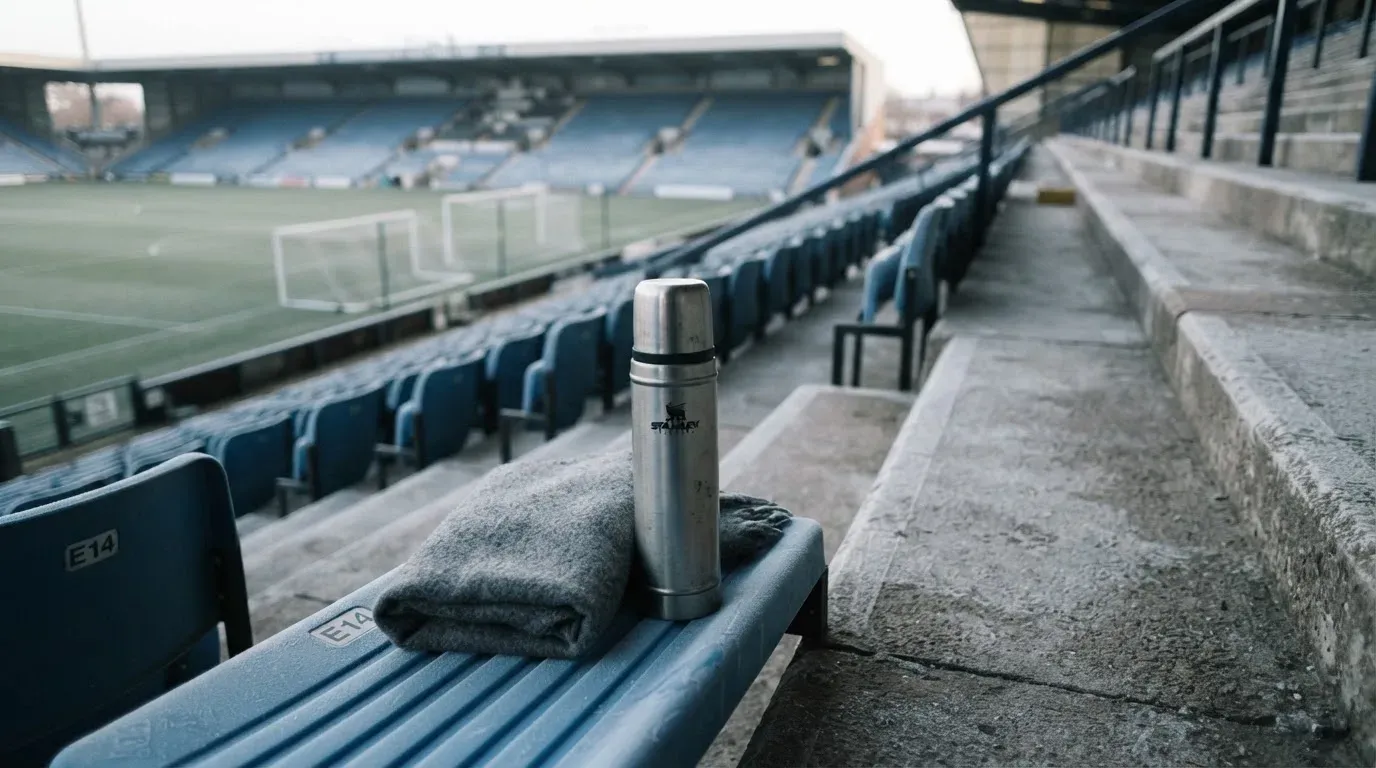 Ein grauer Wollschal und eine Thermoskanne liegen auf einem Sitz im winterlichen Stadion, Raureif liegt auf den Stufen.